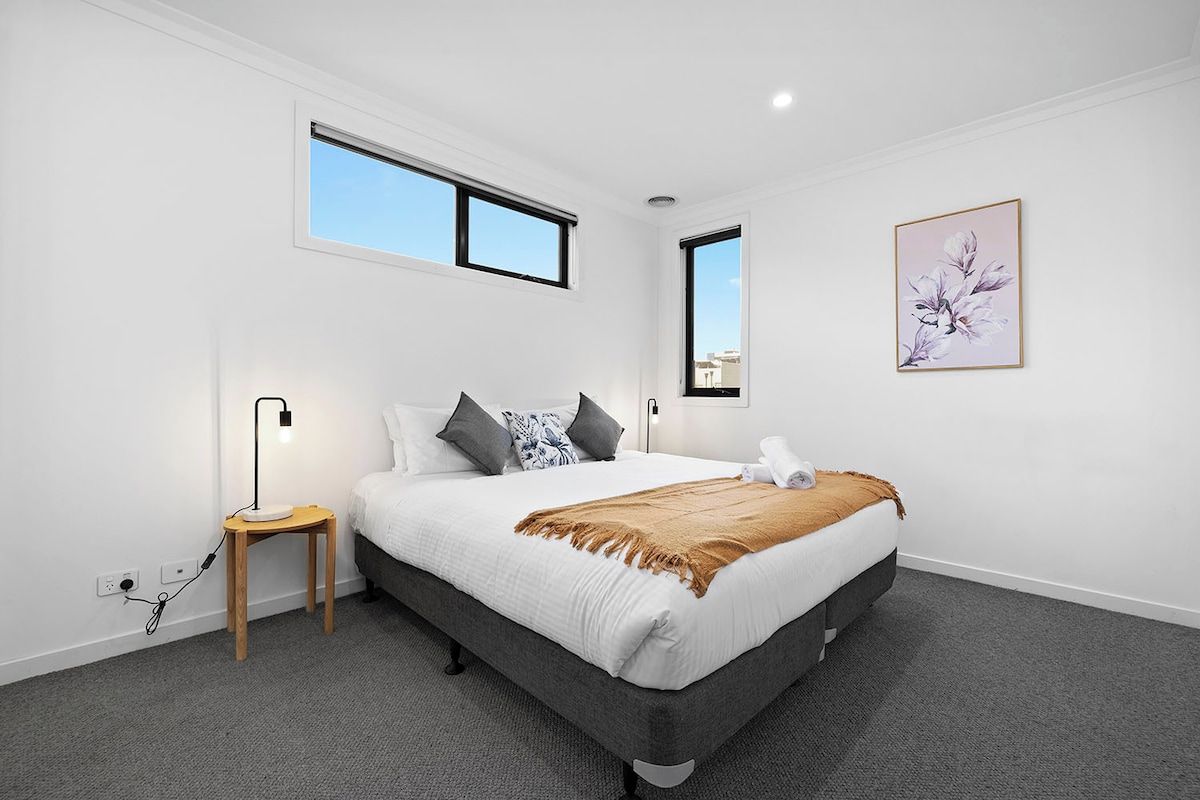 A bedroom with a bed, bedside table, lamp, and a window.