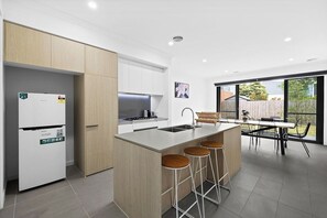 A modern kitchen with a built-in island, bar stools, and a dining area with a view. - Domi Rentals - The Main Residence (Clayton South)
