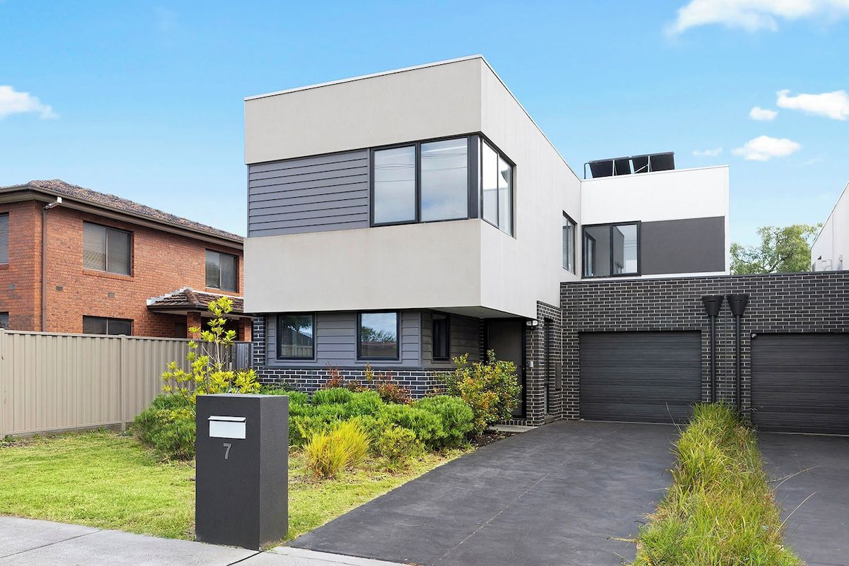 A modern two-story residential building with a garage, a well-maintained lawn, and a mailbox.