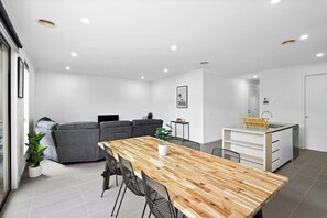 A modern living space with a dining area, a sofa, a kitchen, and a potted plant. - Domi Rentals - The Main Residence (Clayton South)