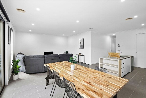A modern living space with a dining area, a sofa, a kitchen, and a potted plant.