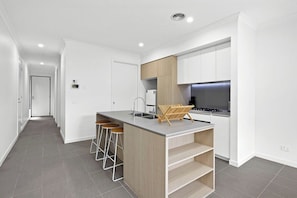A modern kitchen with a central island, bar stools, and a built-in stove.