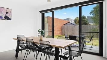 A modern dining area with a wooden table and black chairs, large sliding glass doors leading to a backyard.