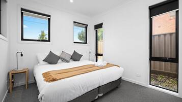 A bedroom with a large bed, two windows, a bedside table, and a view of the outside.