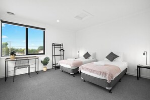A modern bedroom with two beds, a desk, and a window with a view. - Domi Rentals - The Main Residence (Clayton South)