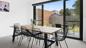 Un espace repas moderne avec une table en bois et des chaises noires, de grandes portes-fenêtres coulissantes donnant sur un jardin.