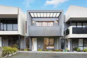 Ein modernes, mehrstöckiges Gebäude mit flachem Dach, großen Fenstern und einem Balkon.