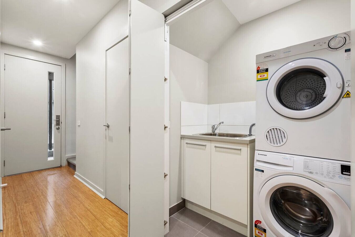 A laundry room with a washing machine, a sink, and a door leading to a hallway.