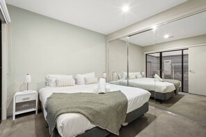 Ein modernes Schlafzimmer mit zwei Betten, einem Nachttisch, einer Lampe und einem großen Spiegel.