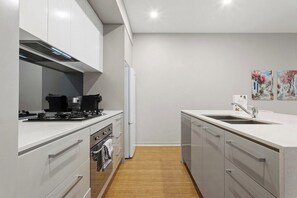 Une cuisine moderne avec des meubles blancs, une cuisinière en acier inoxydable et un four encastré.