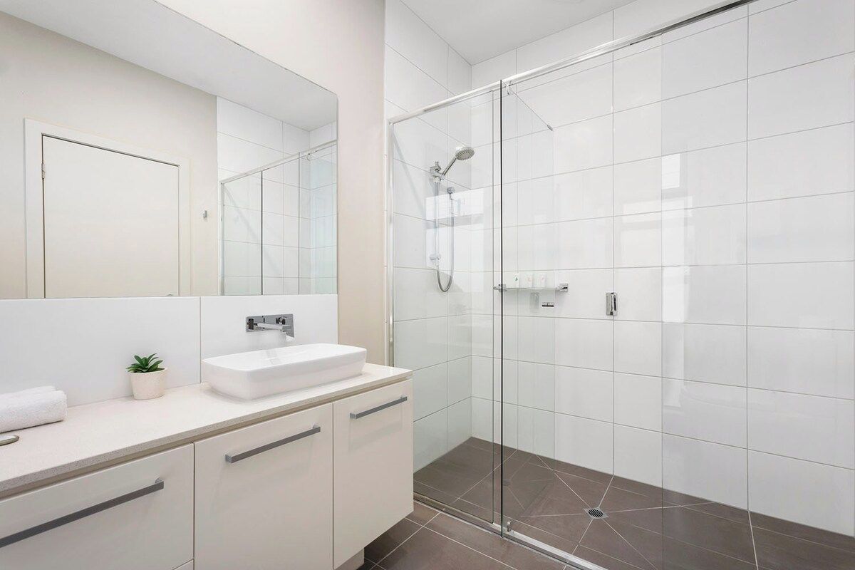 Une salle de bain moderne avec une douche à parois de verre, un lavabo blanc et un grand miroir.