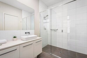 Ein modernes Badezimmer mit Duschkabine aus Glas, einem weißen Waschbecken und einem großen Spiegel.