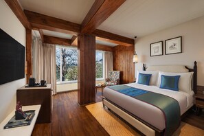 A hotel room with a large bed, wooden beams, a desk with a chair, a TV, and a window with curtains. - Justa Luxe Hollow Oak Mussoorie (Dehradun)