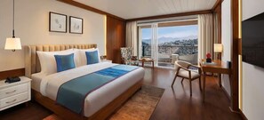 Une chambre d’hôtel avec un grand lit, un bureau, une chaise, un téléphone, une télévision et un balcon avec vue.