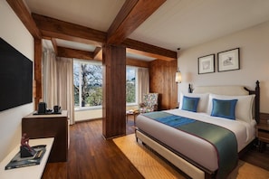 Ein Hotelzimmer mit einem großen Bett, Holzbalken, einem Schreibtisch, einem Sessel und einem Fenster mit Blick.