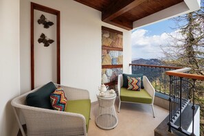 A balcony with wicker chairs, a small table with a teapot, and a stone wall. - Justa Luxe Hollow Oak Mussoorie (Dehradun)