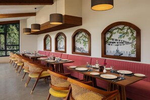 A restaurant with wooden tables and chairs, a pink booth seating area, and framed artwork on the walls. - Justa Luxe Hollow Oak Mussoorie (Dehradun)