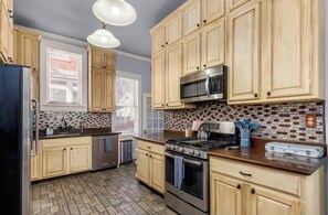 A kitchen with wooden cabinets, a stainless steel refrigerator, a microwave, a stove, and a tiled backsplash. - Historic House Near Downtown and the Riverwalk (San Antonio)