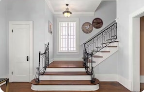 A staircase with ornate black railings, a white door, and a window with blinds. - Historic House Near Downtown and the Riverwalk (San Antonio)