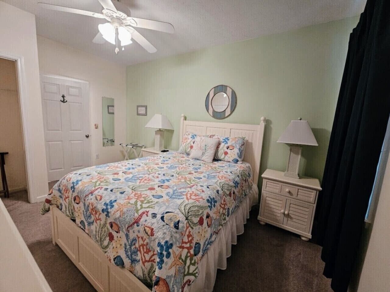 Quarto com cama, mesas de cabeceira, cômoda, ventilador de teto e uma porta.