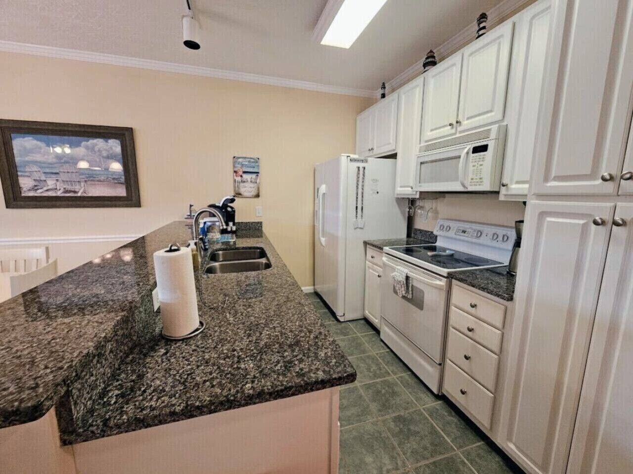 A kitchen with white cabinets, a granite countertop, a refrigerator, a microwave, and a stove.