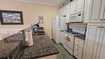 A kitchen with white cabinets, a granite countertop, a refrigerator, a microwave, and a stove.