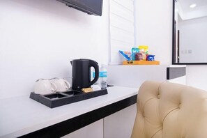 Habitació d'hotel amb un taulell negre i blanc, una cafetera negra, un búllet blanc, una ampolla d'aigua i una cadira beix.