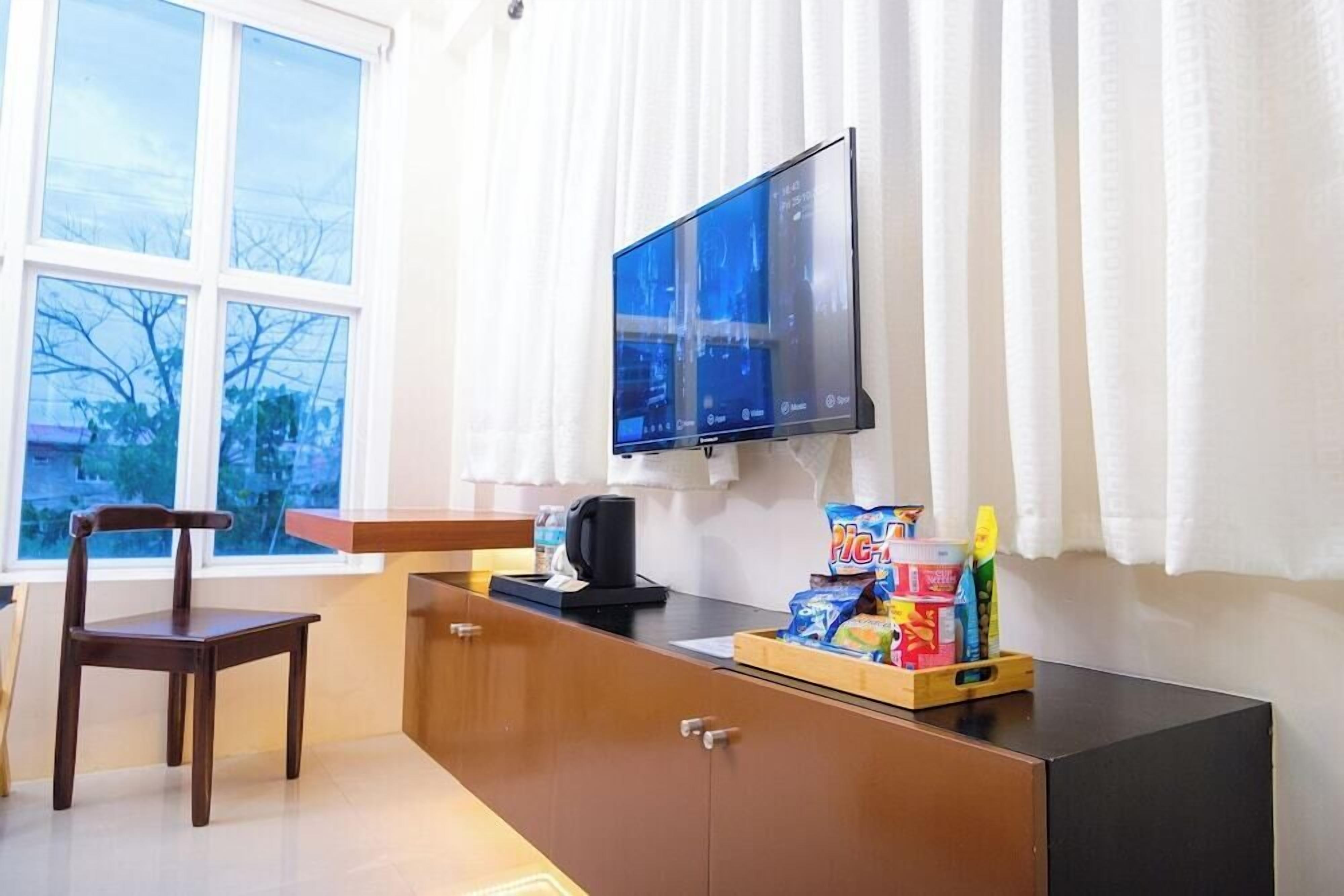 Una habitación con un escritorio de madera, una silla, un televisor montado en la pared y una ventana con cortinas.