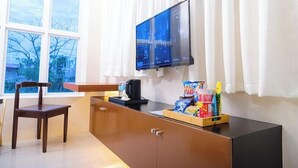 A room with a wooden desk, a chair, a television mounted on the wall, and a window with curtains. - Le Dream Hotel (Vigan)