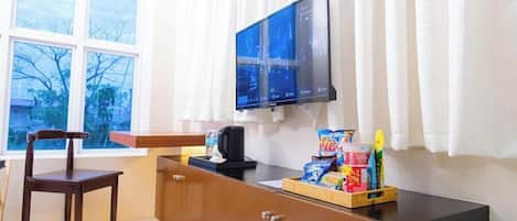 Una habitación con un escritorio de madera, una silla, un televisor montado en la pared y una ventana con cortinas.