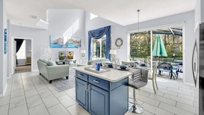 A modern kitchen with a central island, a dining area with outdoor seating, and a living room with a sofa and TV. - 6 bedroom 6 Bath Palm Paradise close to Orlando Theme Parks (Kissimmee)