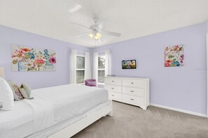 Ein Schlafzimmer mit einem Bett, einer Kommode, einem Deckenventilator und floralen Bildern an den Wänden.