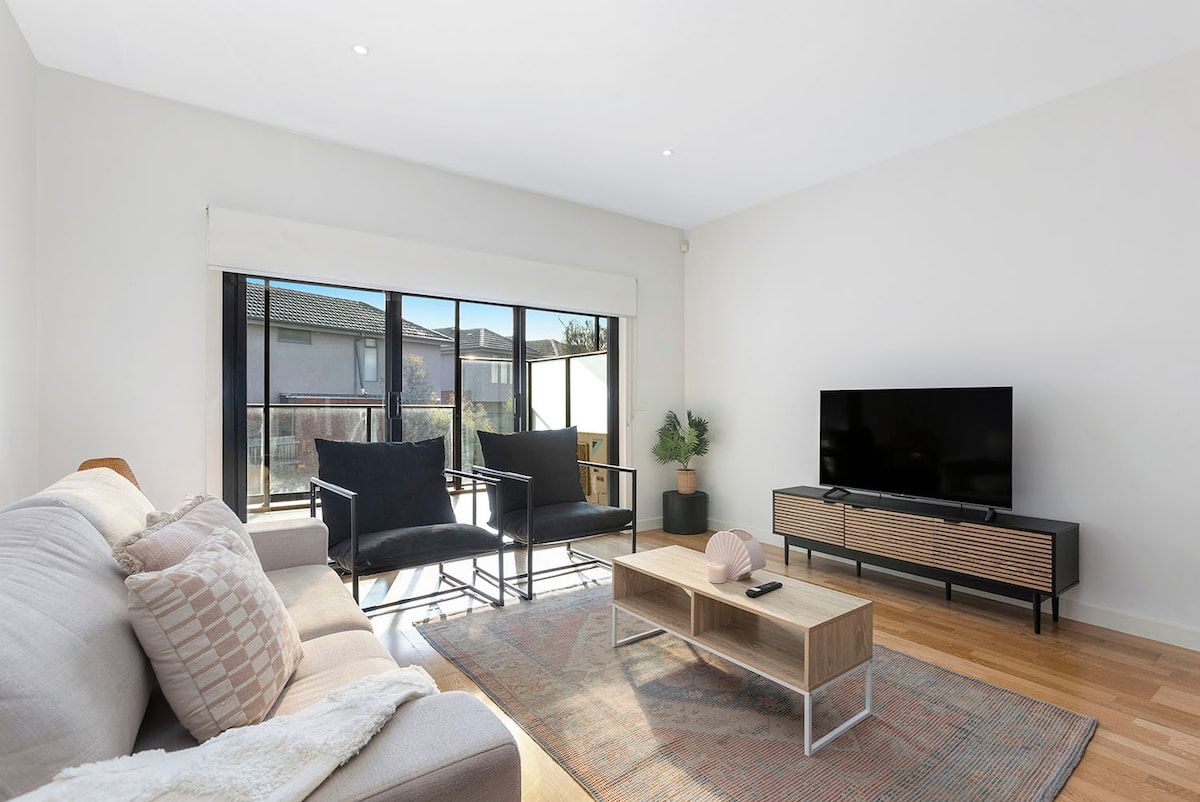 Een moderne woonkamer met een bank, twee fauteuils, een salontafel, een televisie en een groot raam.