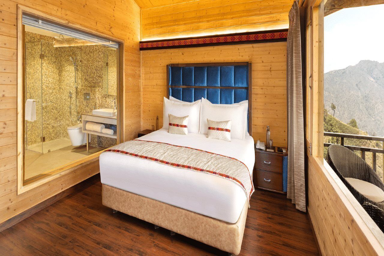Un dormitorio con una cama grande, un baño con cabina de ducha de vidrio y un balcón con vistas a las montañas.