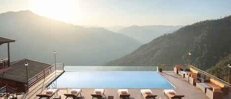A pool area with lounge chairs and a view of mountains.