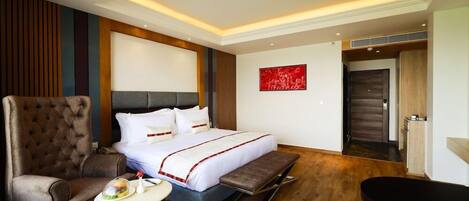 A hotel room with a bed, a chair, a small table, and a bench.
