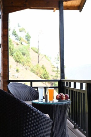 A balcony with wicker furniture, a glass table, and a view of a hillside. - Justa Luxe Cliffend Resort and Spa Mashobra (Shimla)