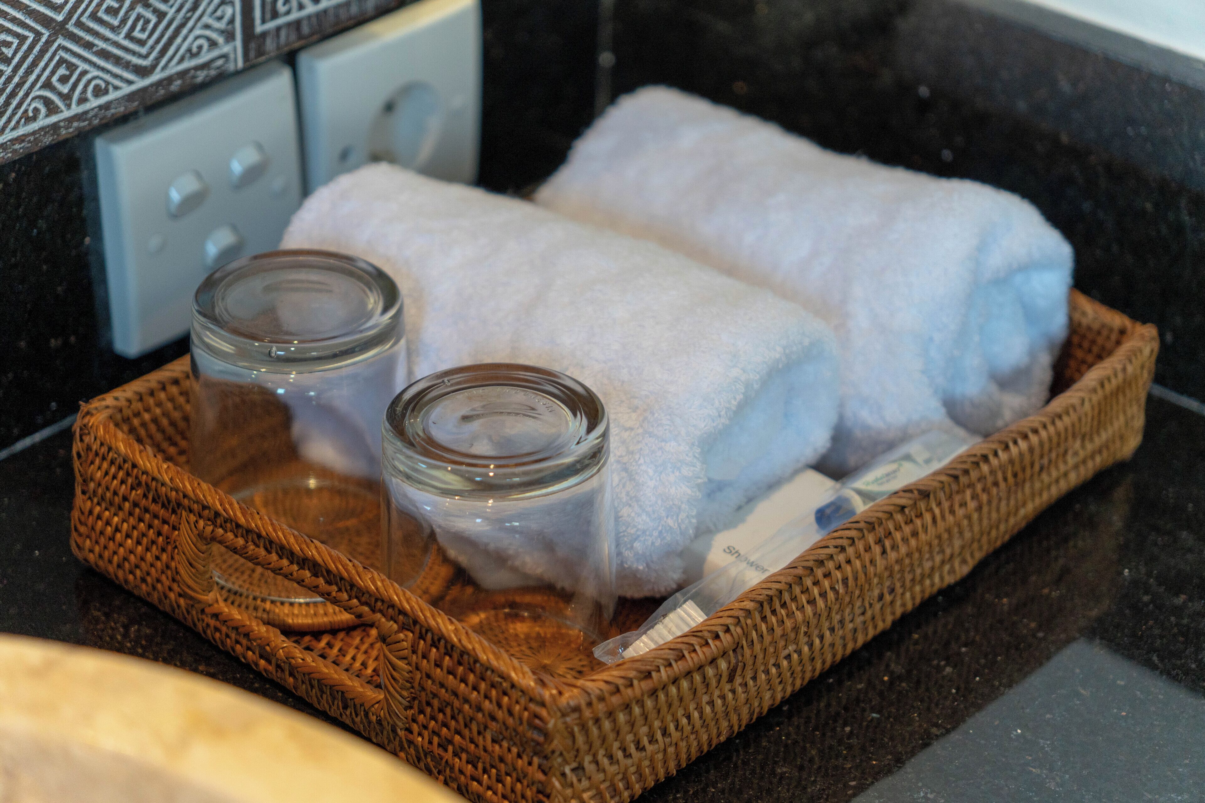 A wicker basket containing two rolled towels and two glass jars on a countertop.