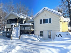 A two-story house with a covered porch and a snow-covered roof. - Lakefront Hot Tub Retreat w/ Mega Arcade (Baxter)
