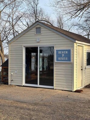A small building with a sign reading 'BEACH HOUSE' and a sliding glass door. - Lakefront Hot Tub Retreat w/ Mega Arcade (Baxter)
