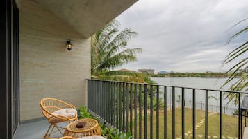 Ein Balkon mit Korbstühlen, einem kleinen Tisch und Blick auf ein Gewässer sowie entfernte Gebäude.