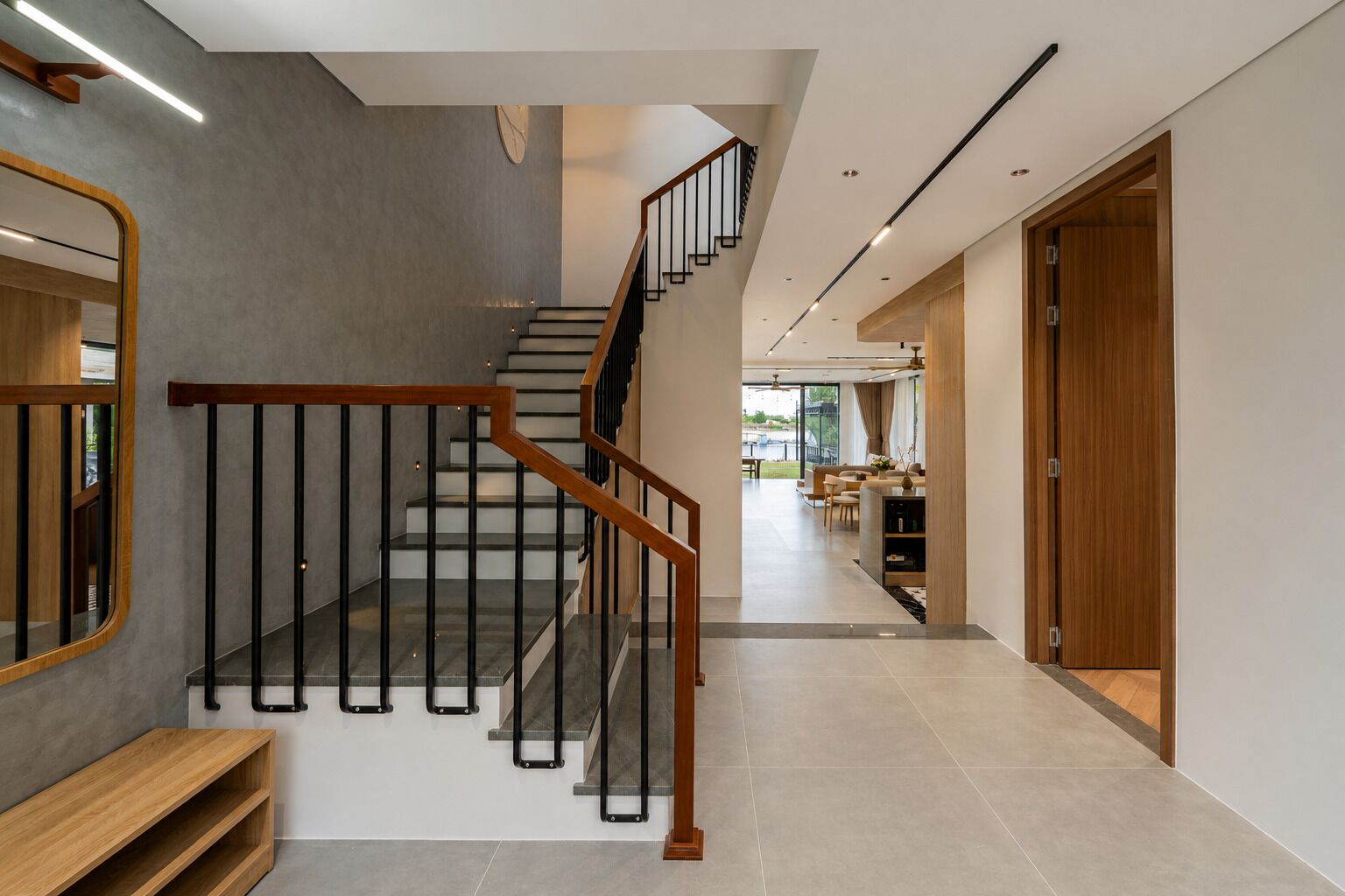 Una escalera moderna con barandas de madera y balaustradas de metal negro, que conduce a una sala de estar con un sofá y una mesa de centro.