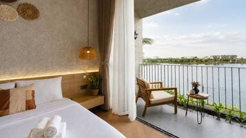 A bedroom with a bed, bedside table, lamp, and a view of a body of water.