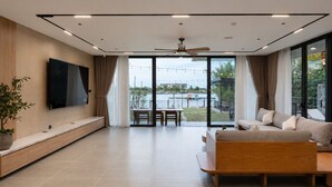 Uma sala de estar moderna com televisão de tela plana, um sofá, uma mesa de jantar e vista para a água.