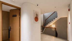 Um corredor com uma porta de madeira identificada com '203 Wind room', uma escada com guarda-corpo de metal e uma obra de arte pendurada na parede.
