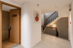 A hallway with a wooden door labeled '203 Wind room,' a staircase with a metal railing, and a wall-mounted artwork. - GiaLinh Villa Hoi An - 5BR - River view (Hoi An)