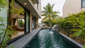 Piscina com cascata, cercada por um edifício moderno com amplas janelas e área de estar externa.