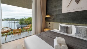 Quarto de hotel com varanda, cama com almofadas, mesa de cabeceira e luminária na parede.
