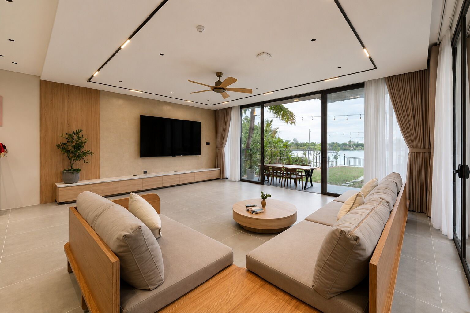 A modern living room with a flat-screen TV, a ceiling fan, a dining area with a table and chairs, and a large window with a view of the outdoors.