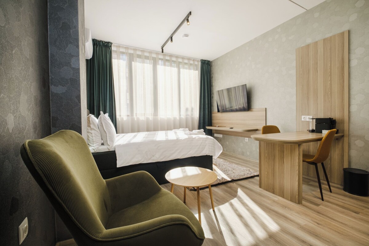 A modern hotel room with a bed, a desk, a chair, and a television.
